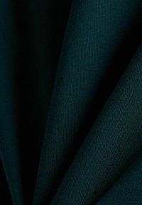 Tejido verde oscuro con una textura suave y un fino patrón acanalado, doblado para revelar capas y profundidad.