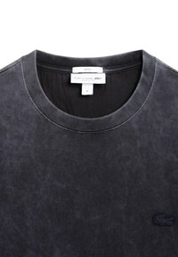 Camiseta negra de cuello redondo hecha de algodón. Presenta una superficie texturizada y un pequeño logo bordado en hilo oscuro en la parte frontal.