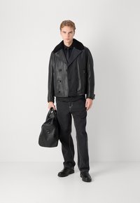 Musta nahkainen kaksirivinen takki, jossa on karvakaulus, yhdistetty mustiin farkkuihin ja mustaan nahkalaukkuun, käytetty mustien kenkien kanssa.