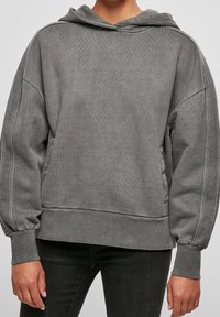 Sweat-shirt gris avec capuche, présentant une texture douce, des épaules tombantes, des poignets côtelés et des poches latérales. Design simple et décontracté.