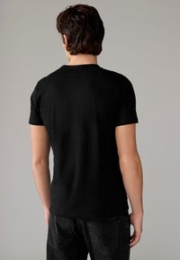 T-shirt nera a maniche corte con collo tondo, realizzata in cotone morbido, caratterizzata da un design semplice e una vestibilità regolare. Sono visibili jeans in denim neri.