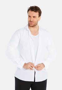 White long-sleeve button-up shirt in smooth fabric, with a classic collar and a relaxed fit, worn open over a white undershirt.