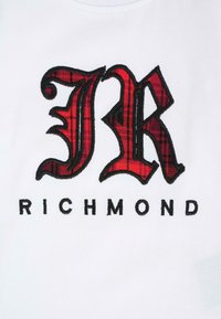 T-shirt in tessuto bianco con un grande logo ricamato tartan rosso e nero "JR" sopra il testo "RICHMOND" in lettere nere.