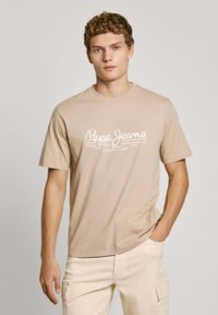 Bežs kokvilnas T-krekls ar īsām piedurknēm un apaļu kakla izgriezumu, kuram priekšpusē ir balti drukāti burti "Pepe Jeans".