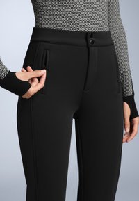 Fekete nadrág sima, rugalmas anyagból, két oldalsó zsebbel, cipzárral és dupla gombos záródással a deréknál.