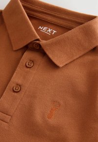 Polo marrone con colletto, tre bottoni marroni e tessuto testurizzato; presenta un logo di aragosta ricamato sul petto.