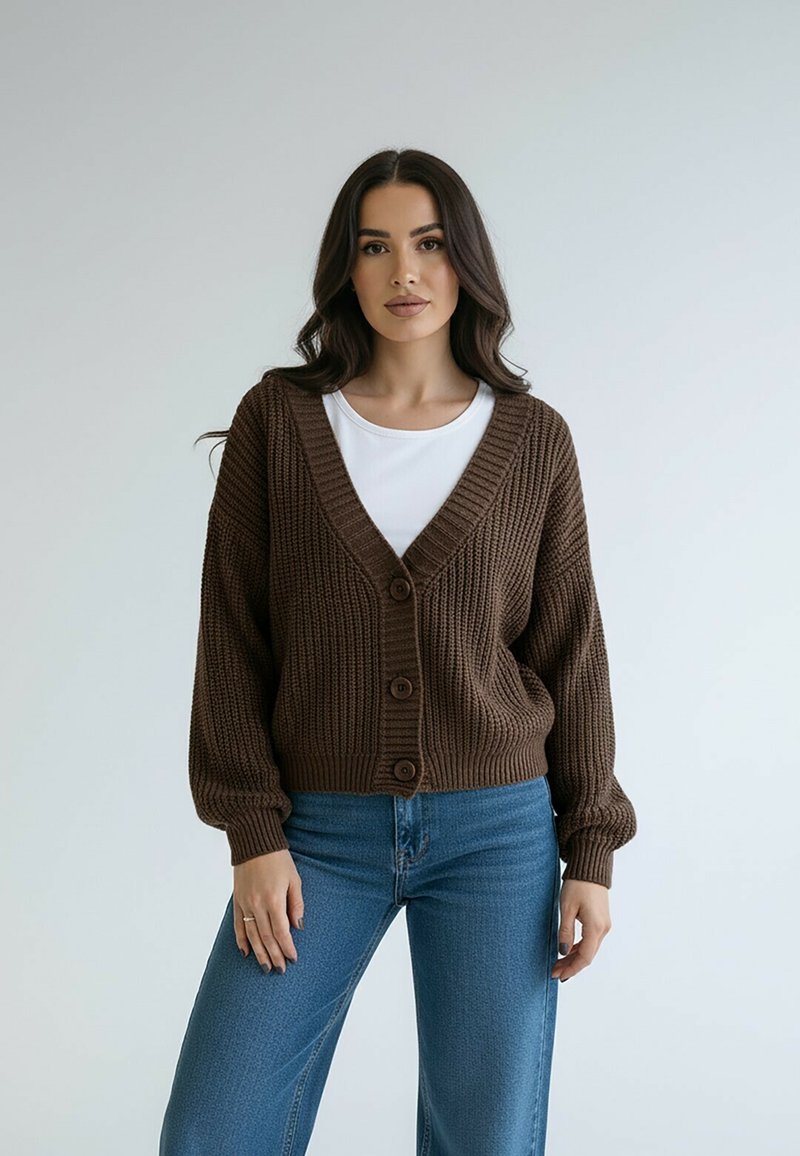 Brązowy dzianinowy kardigan z głębokim dekoltem w kształcie litery V, zapinany na guziki z przodu i zakończony ściągaczami na mankietach. W połączeniu z jasnoniebieskimi dżinsami tworzy casualowy look.