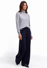 Grauer, gerippter Rollkragenpullover kombiniert mit weiten, dunkelblauen Hosen. Weiches Material mit entspanntem Schnitt und minimalen Details.