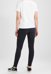 Black skinny jeans with a smooth texture and two back pockets, paired with a plain white t-shirt and black sneakers.