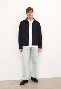 Mustat mokkanahkatakki, valkoinen t-paita, vaaleansiniset farkut ja mustat tennarit. Takissa on napit ja kaulus, ja se on minimalistisessa muodossa.