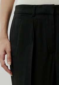 Schwarze, hochgeschnittene Hose mit tailliertem Schnitt, ausgestattet mit zwei Vordertaschen und einer glatten Textur, kombiniert mit einem gerippten weißen Oberteil.