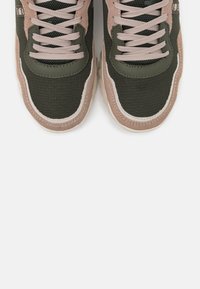 Zelené a béžové sportovní tenisky s prodyšnou tkaninou, polstrovaným jazykem a tkaničkami. Texturovaná podrážka s kontrastními barevnými detaily.