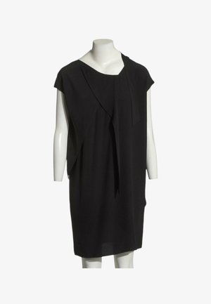 Robe noire sans manches longueur genou avec tissu drapé asymétrique présentée sur un mannequin blanc sur fond blanc.