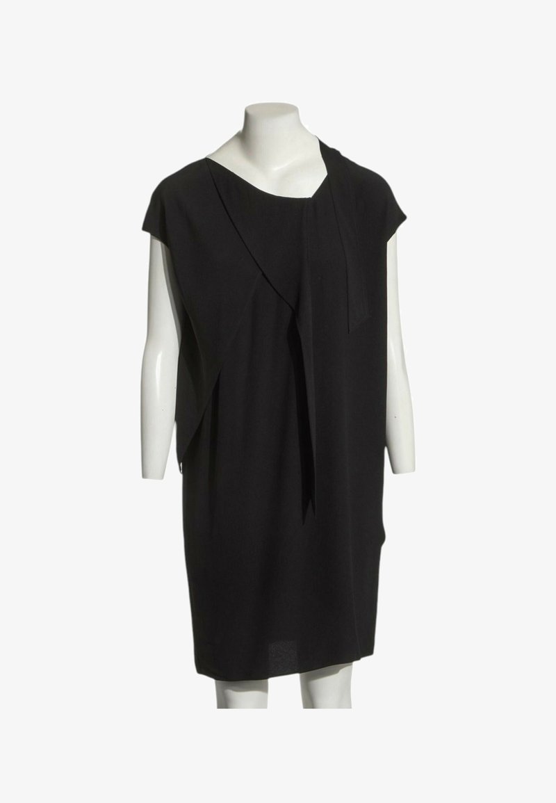 Robe noire sans manches longueur genou avec tissu drapé asymétrique présentée sur un mannequin blanc sur fond blanc.