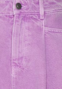 Tela de mezclilla de color púrpura claro con un acabado texturizado, que presenta un botón metálico, costuras cosidas y un detalle de bolsillo lateral.