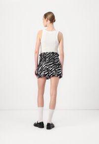 Biely top bez rukávov skombinovaný s sukňou v čierno-bielom pruhovanom vzore zebra, so skráteným lemom, obutý s čiernymi topánkami a bielymi krátkymi ponožkami.