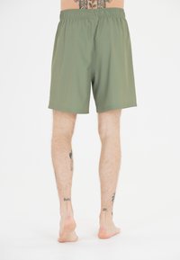 Gröna simbyxor med elastisk midja och lös passform, designade för komfort. Materialet verkar vara lätt och har en mjuk textur.