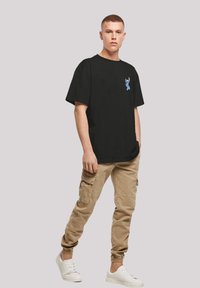 Black cotton t-shirt with short sleeves featuring a blue cartoon character printed on the chest, paired with beige cargo pants and white sneakers.
