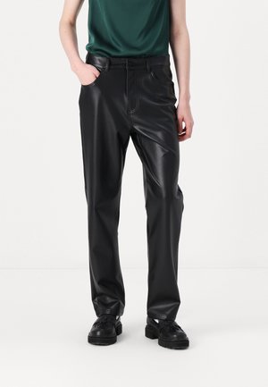 Zwarte faux leren broek met een rechte pasvorm, voorzakken en zichtbare stikdetails. Outfit gestyled met een donkergroen topje en zwarte schoenen.