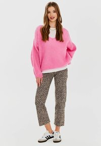 Przesadnie duża różowa sweter z dzianiny, biały top z okrągłym dekoltem, spodenki w panterkę, oraz czarno-białe sneakersy. Luźna stylizacja.