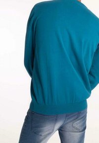 Turkusowy sweter z miękkiej tkaniny o zaokrąglonym dekolcie i ściągaczami przy rękawach, zestawiony z wyblakłymi niebieskimi dżinsami z tylnymi kieszeniami.