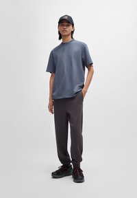 Tricou din bumbac gri și pantaloni jogger gri închis, stilizați cu o șapcă neagră cu un logo rectangular. Material texturat cu o formă relaxată.
