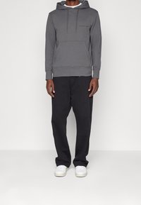 Šedá mikina s kapucí a přední kapsou, s žebrovanými manžetami, spárovaná s černými kalhotami a bílými teniskami. Minimalistický design, bez vzorů.