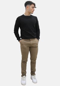 Zwarte longsleeve trui, beige chino's en witte sneakers. Slank fitting ontwerp, gladde textuur en minimale details.