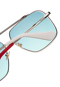 Occhiali da sole con montatura in metallo argentato, lenti blu sfumate, accenti rossi e bianchi sulle aste e para-naso trasparenti per il comfort.