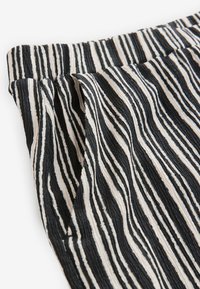 Tessuto a righe verticali bianco e nero con una superficie texture e una fascia elastica in vita, caratterizzato da sottili plissettature.