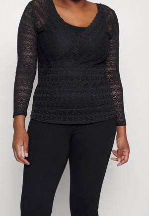 Black long-sleeve lace top with floral patterns worn over a sleeveless black undershirt, paired with black pants.