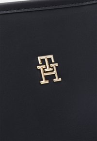 Surface en cuir noir avec un petit logo métallique doré composé des lettres majuscules enchevêtrées T et H.