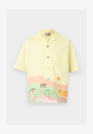 Chemise jaune pâle à manches courtes avec boutons, motif paysage avec des collines, des bâtiments, des arbres et un soleil couchant en bas de l'ourlet.