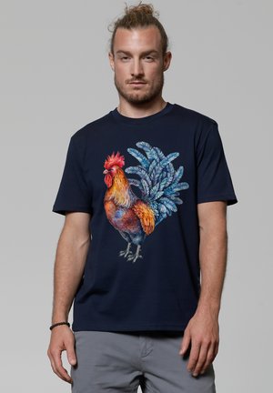 Navy t-shirt featuring a colorful rooster graphic. Short sleeves, crew neckline, cotton material, and detailed feather accents in various shades.