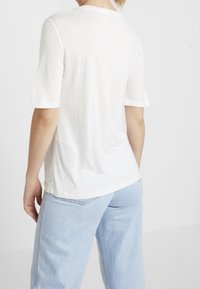 Vit kortärmad t-shirt i lättviktsmaterial, med rund halsringning och avslappnad passform. Synliga sömmar och en slät yta.