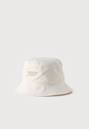 Biely bavlnený klobúk typu bucket s vyšívaným nápisom "tommy jeans" v béžovej farbe na prednej strane, zobrazený na jednoduchom svetlom pozadí.