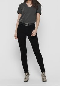Jeans skinny negros combinados con una camiseta de cuello en V gris oscuro. El modelo lleva un cinturón negro con hebilla plateada y botas de tobillo con un diseño.