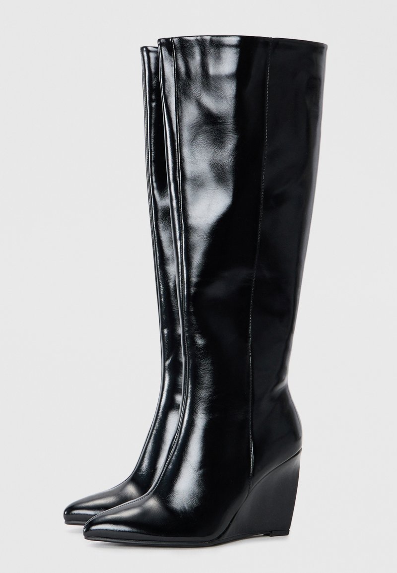 Zwarte leren kniehoge wedge laarzen met een glanzende afwerking, spitse neus en verticale naaddetail op de schacht.