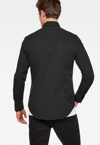 Svart långärmad skjorta i blandad bomull, med spetsig krage, knäppning vid ärmslut och rundad fåll.