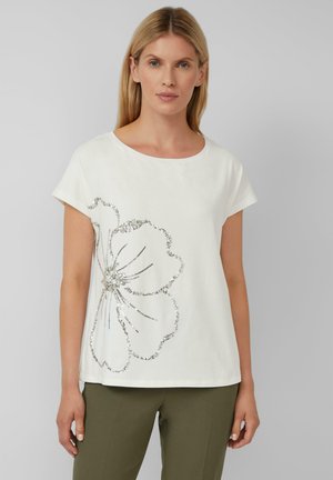 White short-sleeve t-shirt featuring a silver floral design made of sequins, round neck, and a relaxed fit. Paired with olive green trousers.