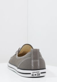 Scarpa slip-on in tela grigia con cuciture bianche, suola in gomma e striscia nera che presenta il marchio "CONVERSE ALL STAR".