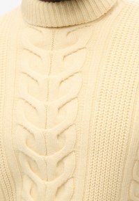 Pull crème en maille torsadée avec col roulé. Présente des motifs texturés et des détails côtelés sur le col et les côtés. Matière en laine douce.