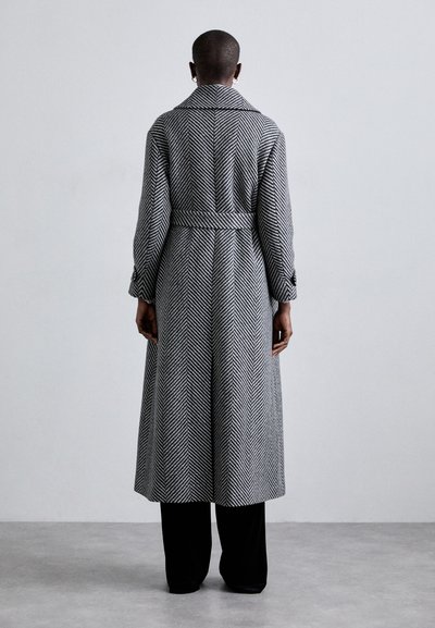 Langer Mantel mit Hahnentrittmuster und tailliertem Gürtel, aus gewebtem Stoff in Schwarz und Grau. Verfügt über einen klassischen Kragen und gekrempelte Ärmel.