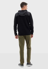 Felpa nera con una parte superiore grigia, abbinata a pantaloni verde oliva. L'outfit presenta un cappuccio con stringa e calzature casual.