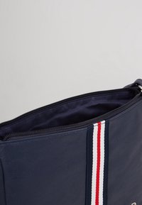 Granatowa skórzana torba z zamknięciem na zamek. Posiada fakturowane wykończenie oraz pionowy wzór w czerwone, białe i niebieskie akcenty.