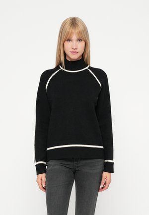 Pull en col roulé noir avec des accents blancs, présentant une coupe décontractée, des poignets et un ourlet côtelé. Texture douce, détail de couture contrastant.
