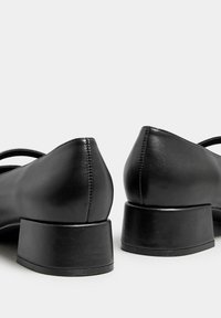 Svarta läderklackskor med rund tå, med en slät finish och synlig sömnad längs sömmen.