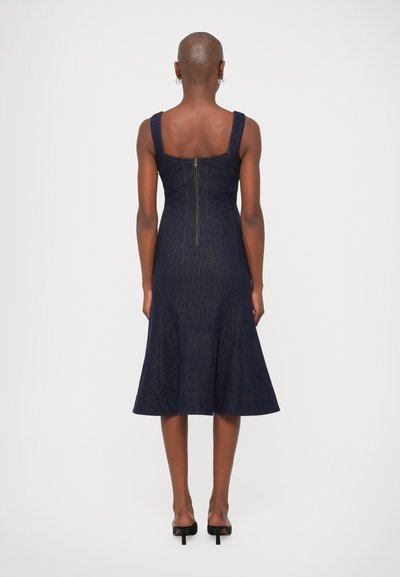 Džínová šaty s priliehavým telovým a rozšírenou sukňou v tmavomodrej farbe. Má široké ramienka a zips na zadnej strane. Hladká textúra.