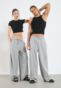 Des tops courts noirs et un pantalon gris ample avec ceinture élastique. Le pantalon a des poches latérales et un tissu léger. Des chaussures noires complètent le look.