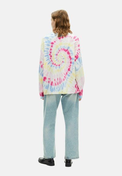 Langearm tie-dye shirt in pastelkleuren van roze, blauw en geel, met een spiraalpatroon, gecombineerd met lichtblauwe high-waisted jeans.